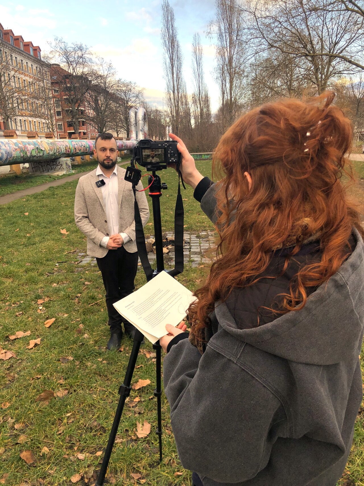 Jugendliche interviewen einen Politiker mit Kamera im Park.